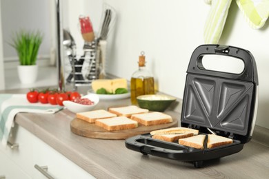 Photo of Modern sandwich maker with bread slices on wooden table in kitchen