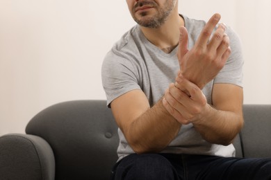 Photo of Man suffering from pain in his hand on sofa indoors, closeup