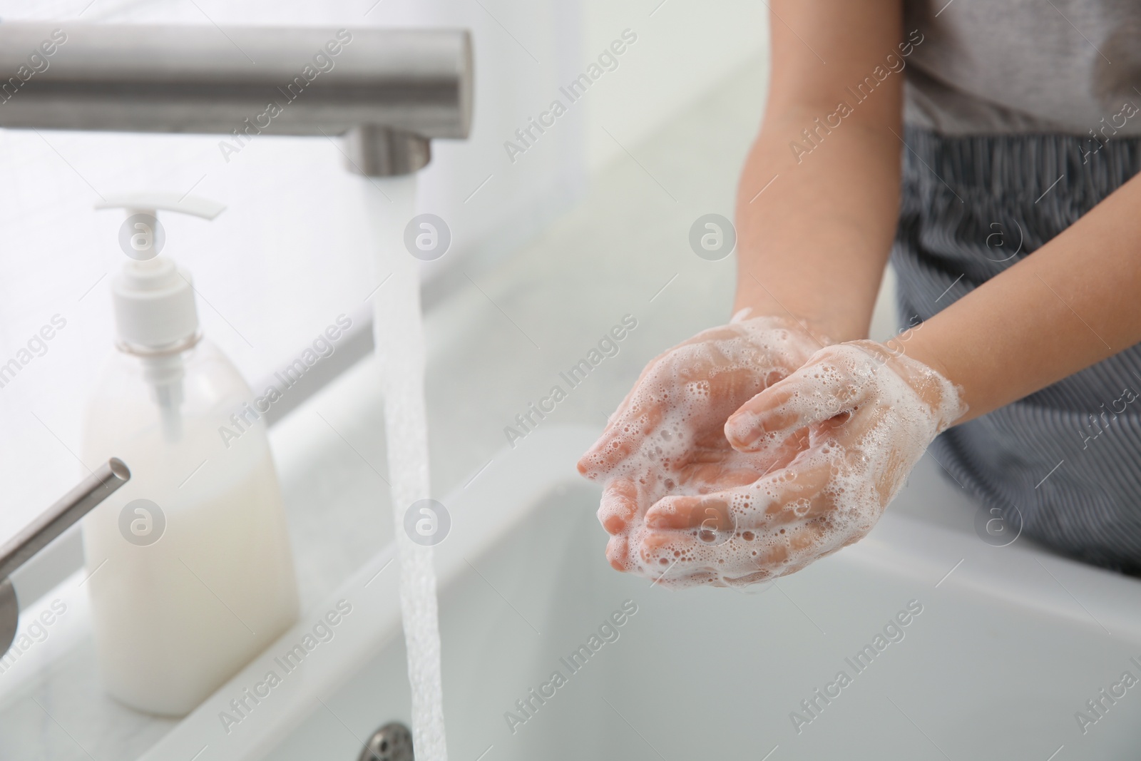 Photo of Little girl washing hands with liquid soap at home, closeup