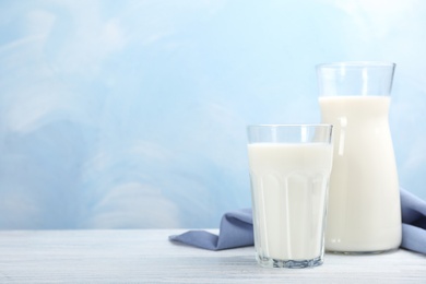 Glass and cruet with fresh milk on table against color background. Space for text