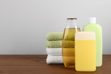 Photo of Different shower gel bottles with towels on wooden table. Space for text