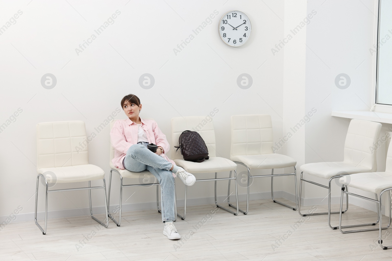 Photo of Woman with cup of drink waiting for appointment indoors