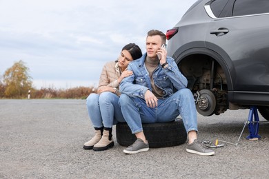 Photo of Young man calling to car service on roadside. Tire puncture