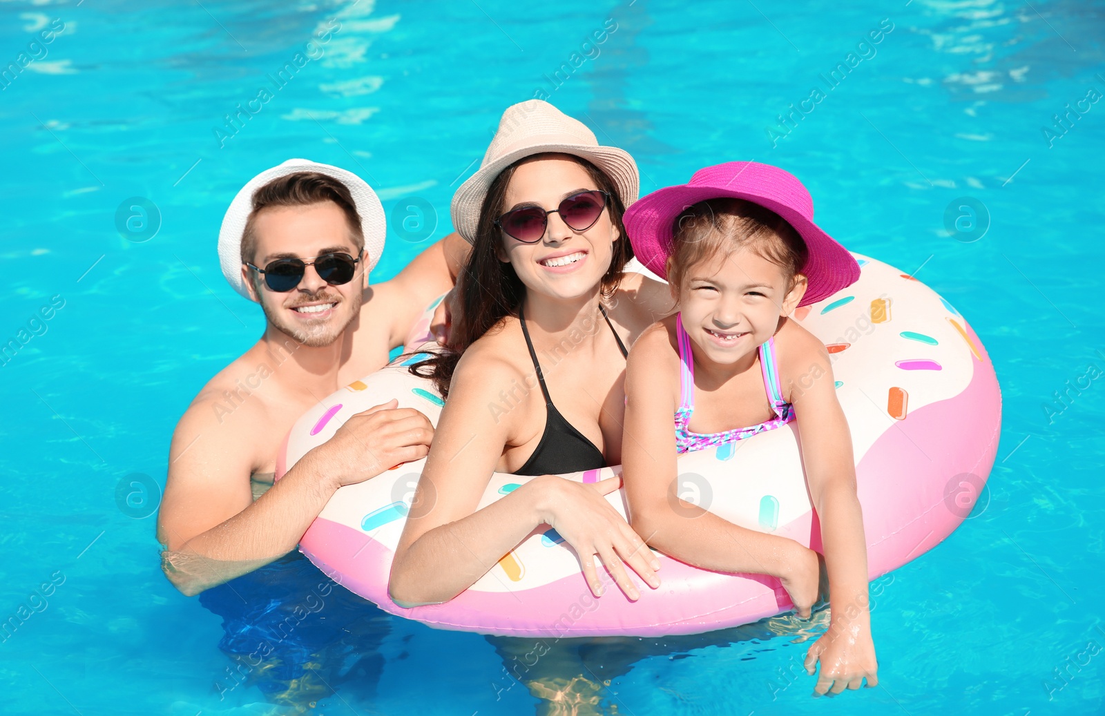 Photo of Young family with little daughter in swimming pool on sunny day