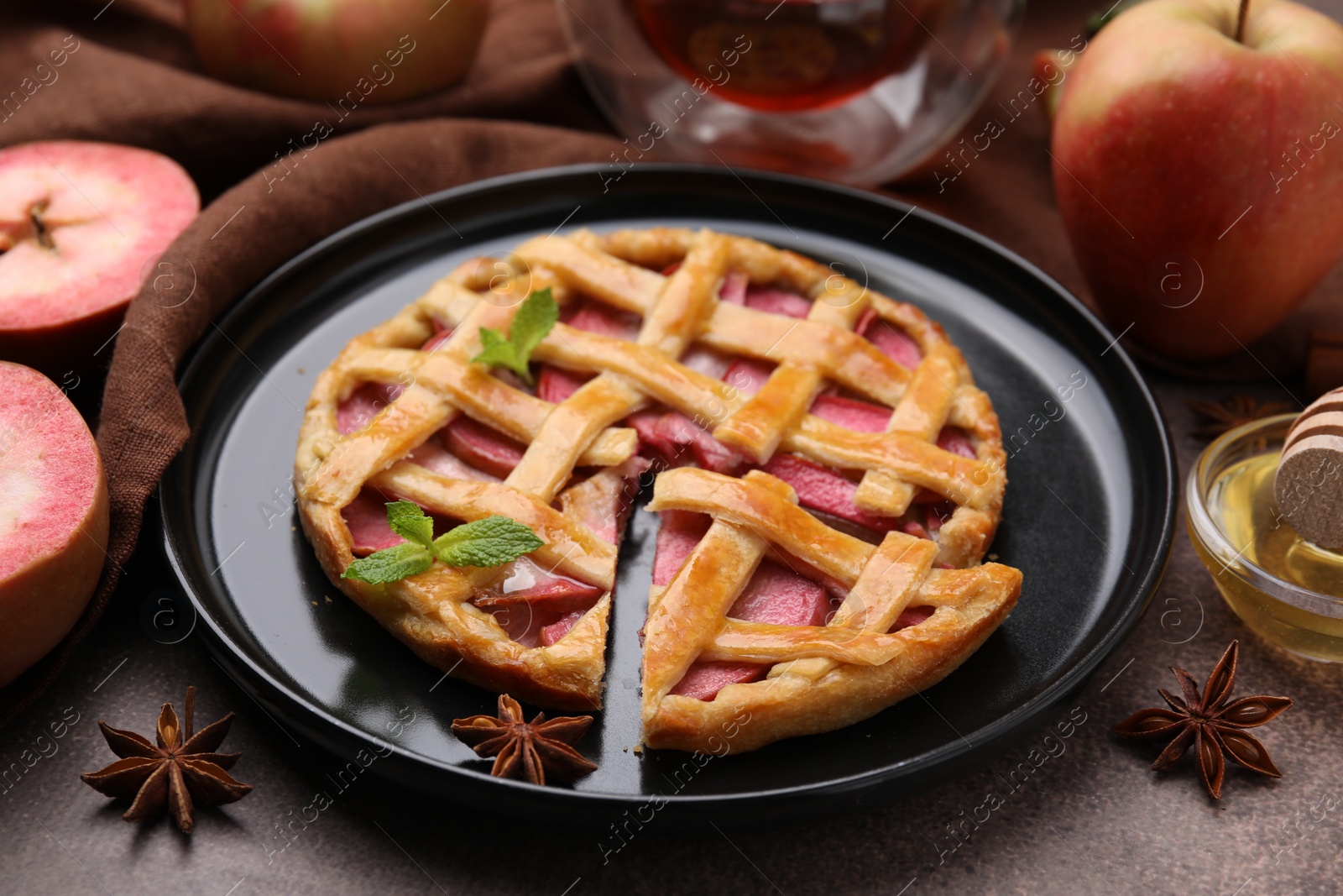 Photo of Delicious apple pie with mint and ingredients on brown table