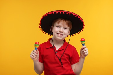 Photo of Cute boy in Mexican sombrero hat with maracas on yellow background