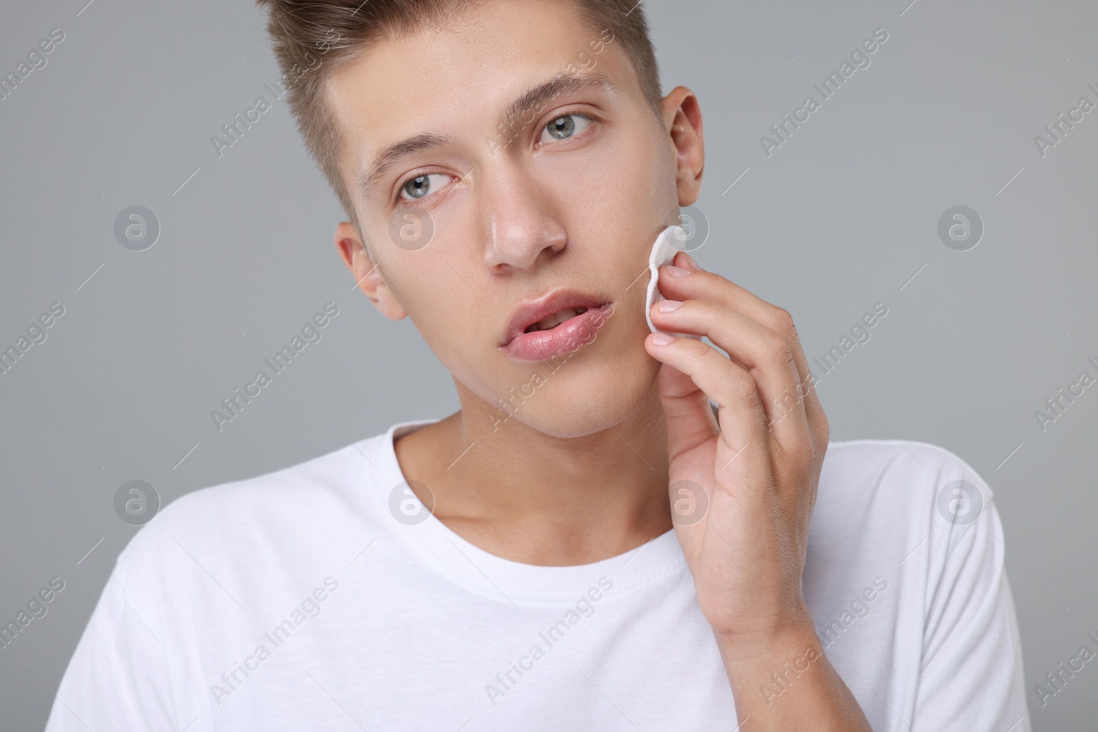 Photo of Handsome man cleaning face with cotton pad on grey background