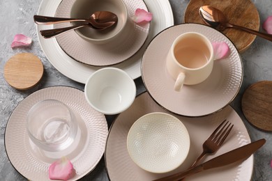 Stylish table setting. Dishes, cutlery, cup and petals on grey surface, above view