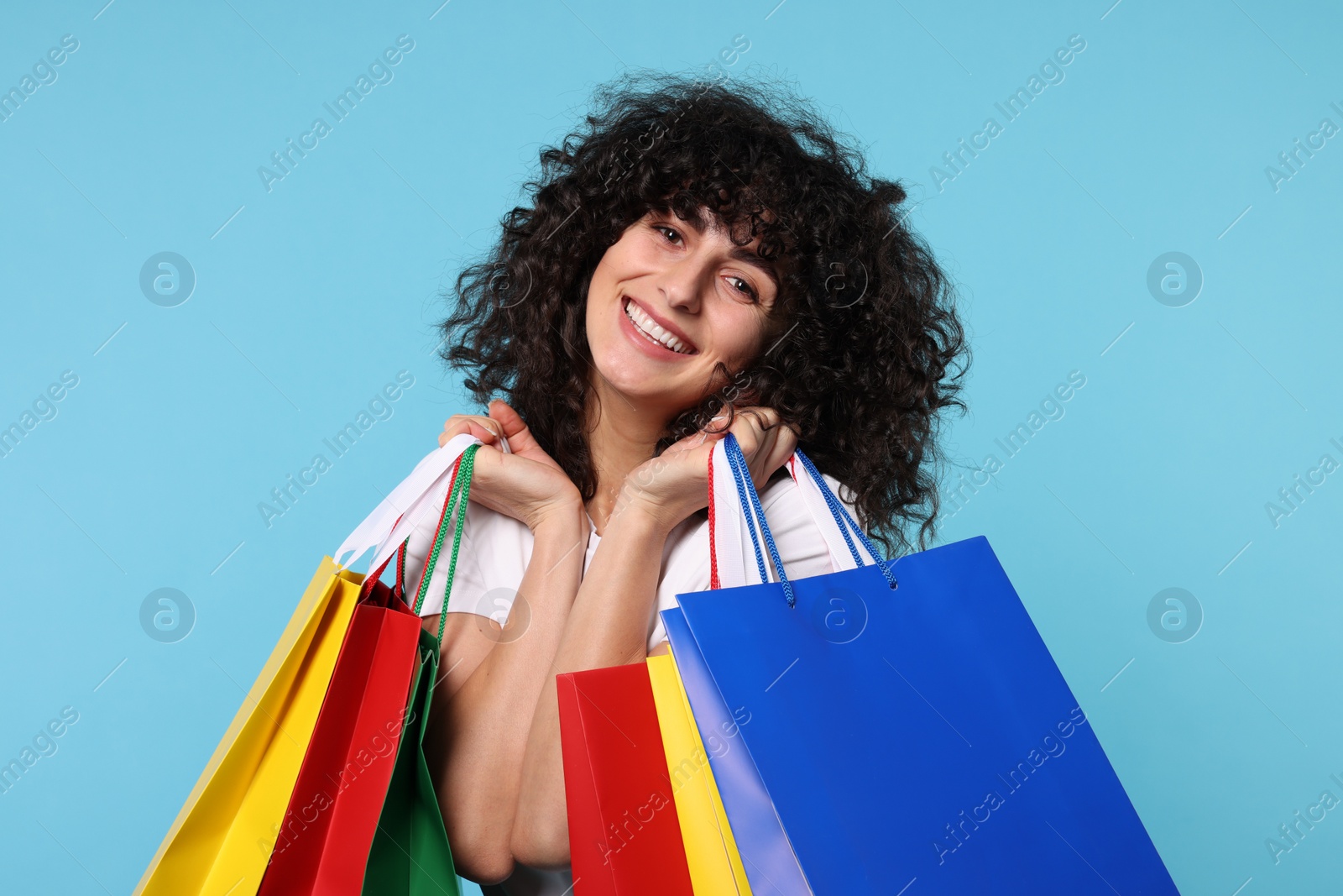 Photo of Happy young woman with shopping bags on light blue background