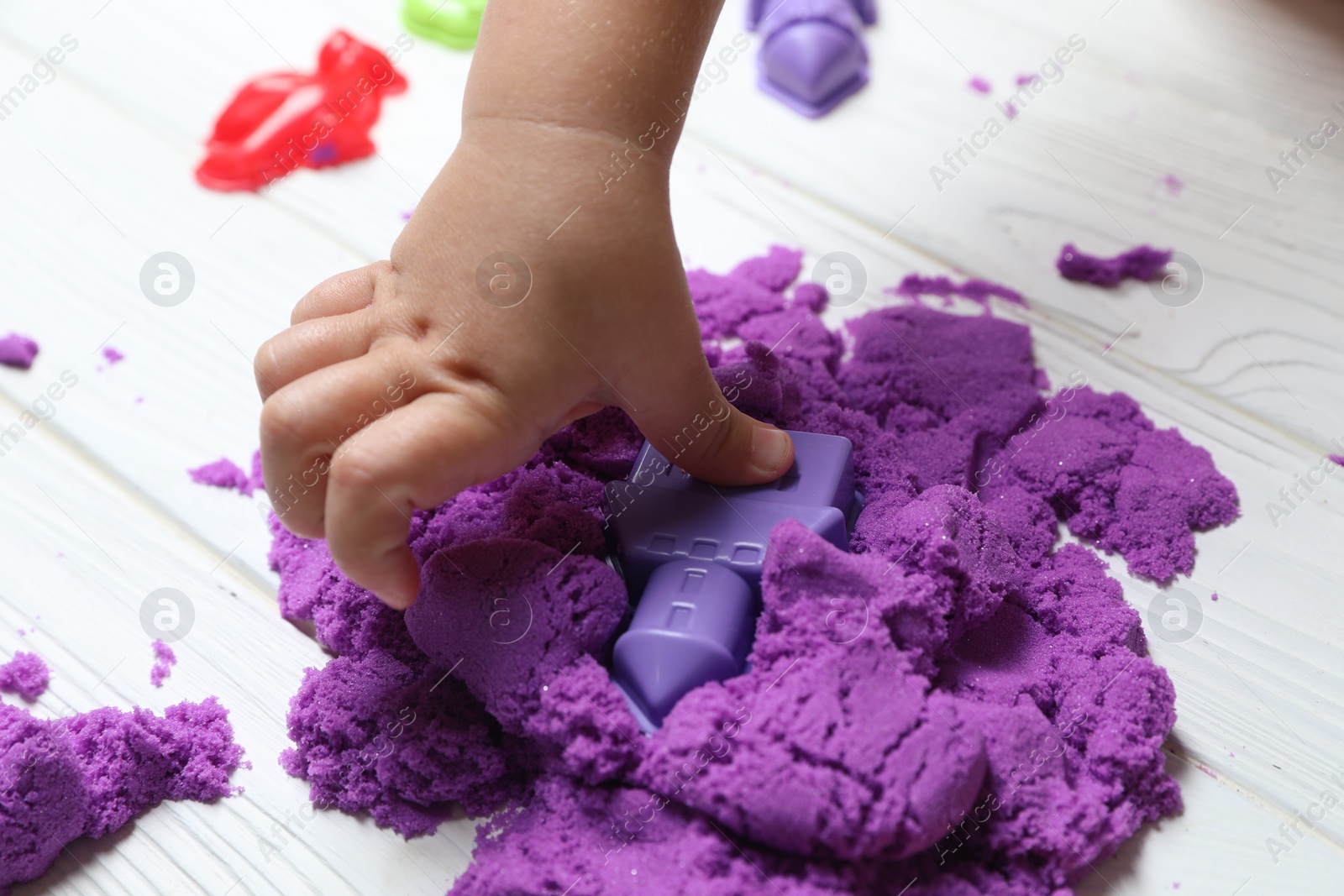 Photo of Little child playing with kinetic sand at white wooden table, closeup