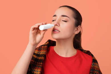 Woman using nasal spray on peach background