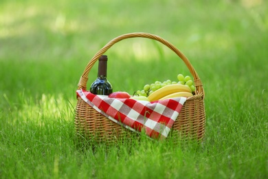 Wicker basket with blanket, wine and food on green grass in park. Summer picnic