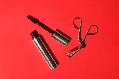 Black mascara and eyelash curler on red background, flat lay. Makeup product