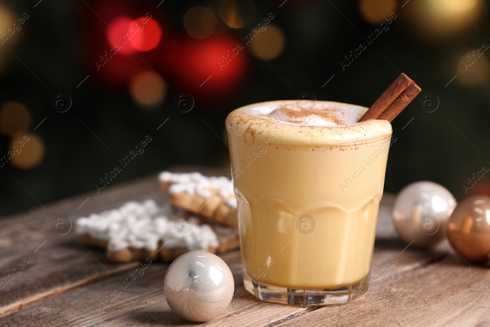 Photo of Tasty eggnog with cinnamon, cookies and baubles on wooden table against blurred festive lights. Space for text