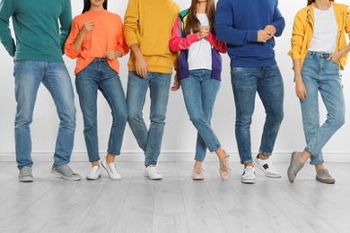 Group of young people in stylish jeans near white wall, closeup