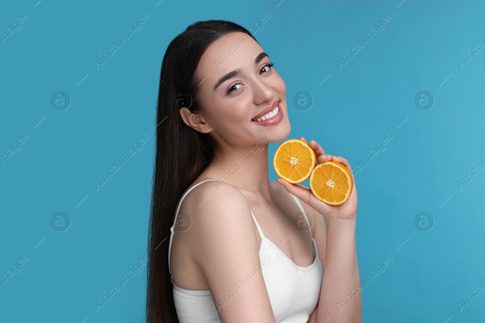 Photo of Beautiful young woman with pieces of orange on light blue background