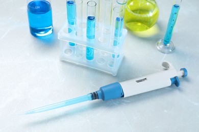 Laboratory analysis. Micropipette and different glassware with liquids on light grey marble table