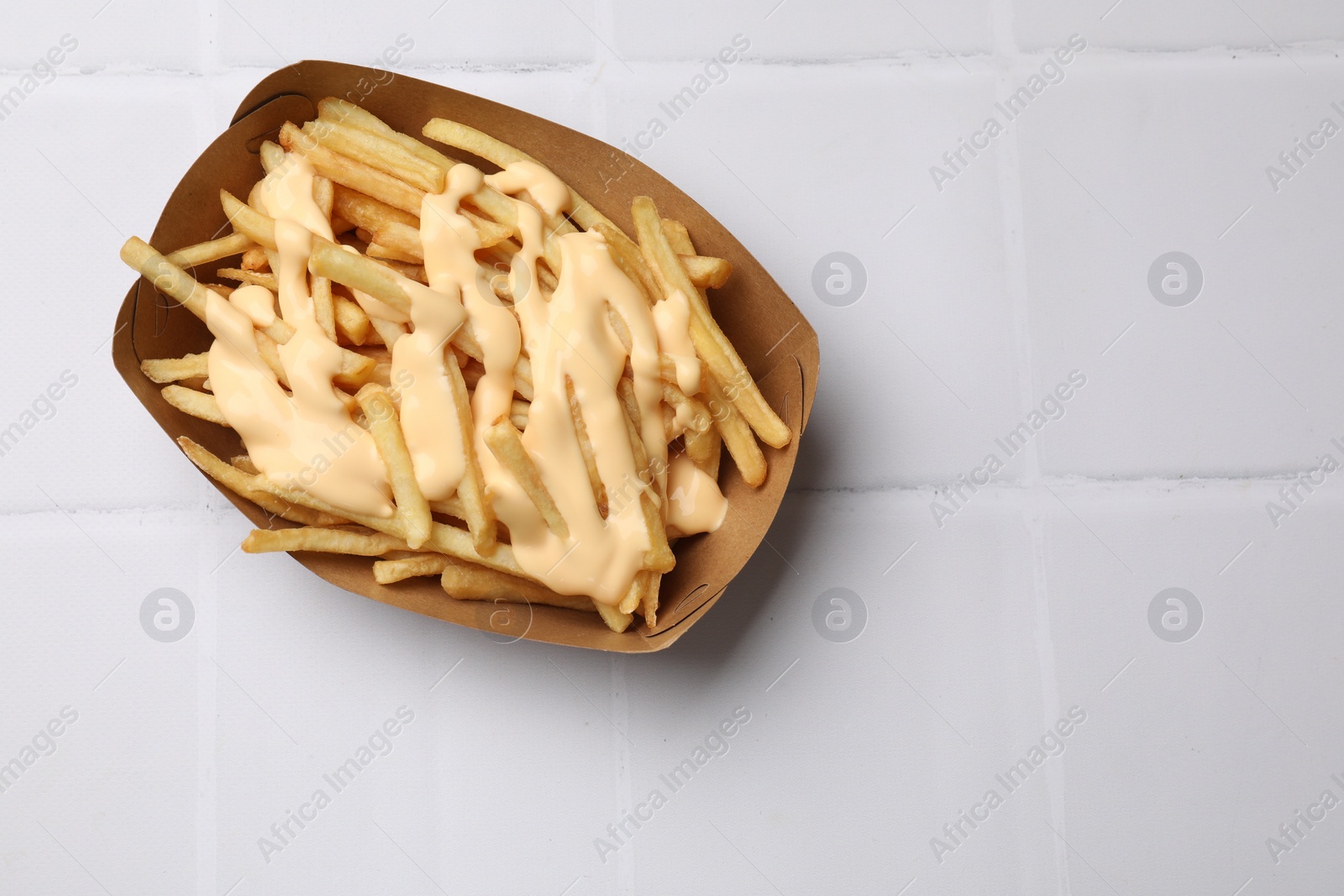 Photo of Delicious French fries with cheese sauce on white tiled table, top view. Space for text