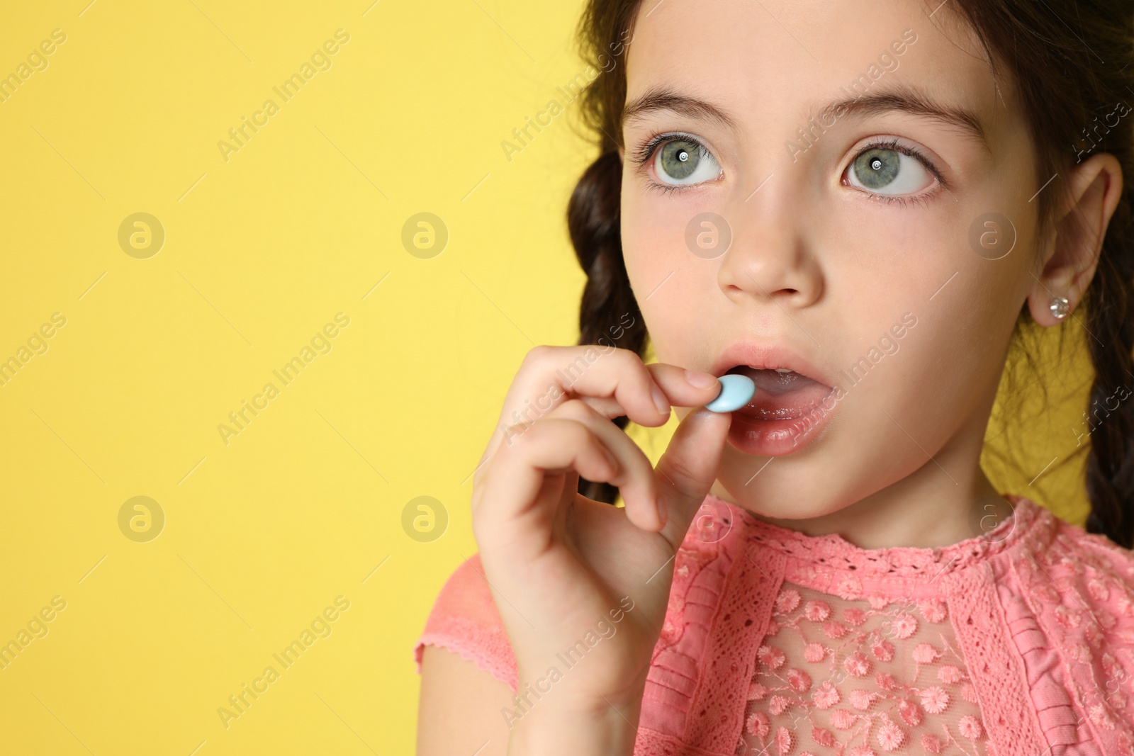 Photo of Little girl taking vitamin pill on yellow background, closeup. Space for text