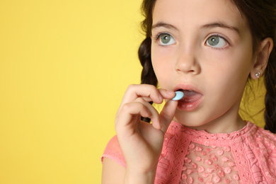 Photo of Little girl taking vitamin pill on yellow background, closeup. Space for text