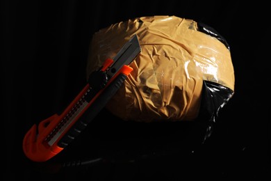 Photo of Smuggling, drug trafficking. Package with narcotics and utility knife on black surface