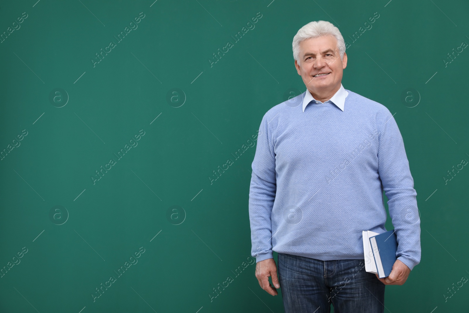 Photo of Portrait of senior teacher with books at green chalkboard, space for text