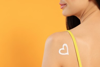Photo of Young woman with heart drawn with sunscreen against orange background, closeup. Space for text