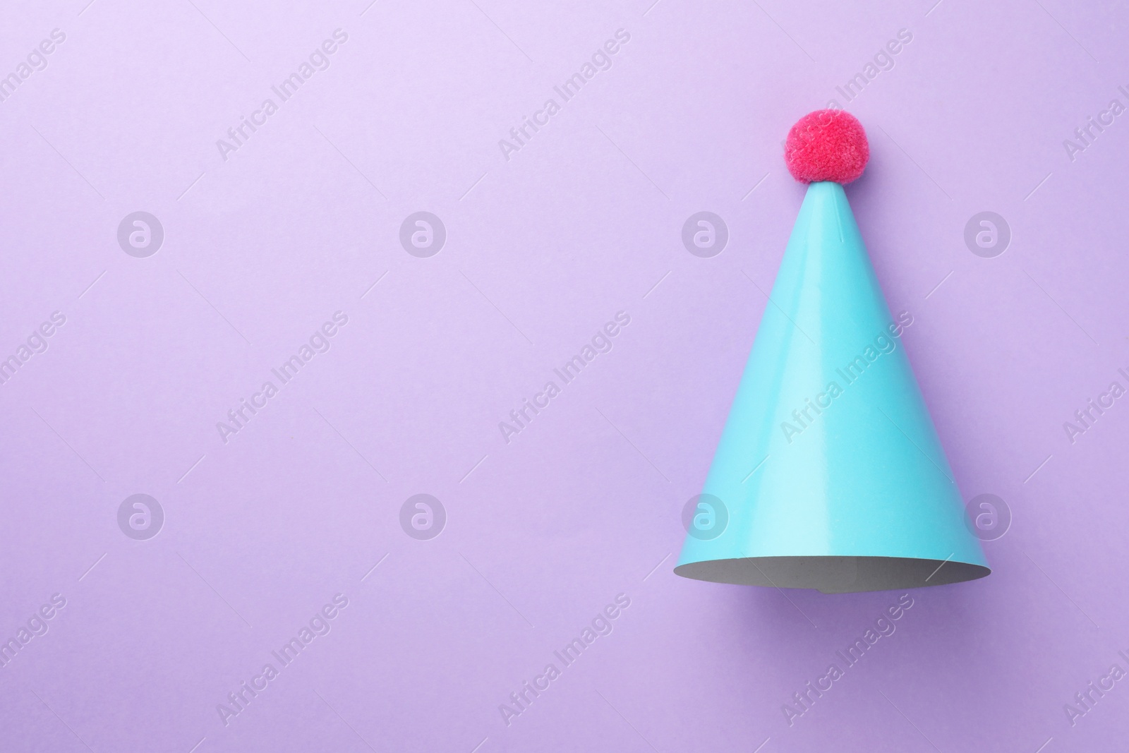 Photo of One light blue party hat with pompom on purple background, top view. Space for text