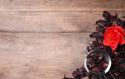 Photo of Dry hibiscus tea, sieve and flower on wooden table, flat lay. Space for text