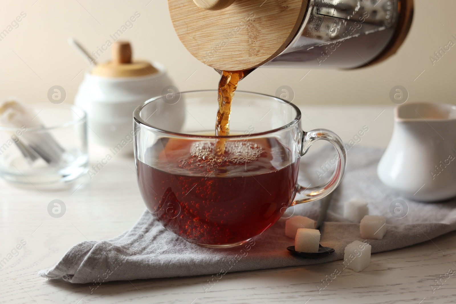 Photo of Pouring warm tea into cup on white wooden table, closeup