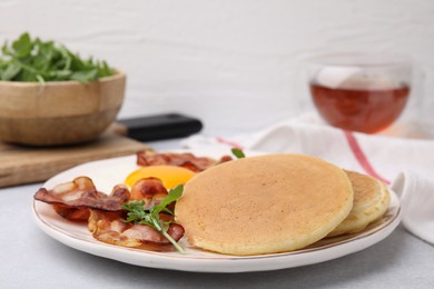 Photo of Plate with tasty pancakes, arugula and bacon on light grey textured table, closeup