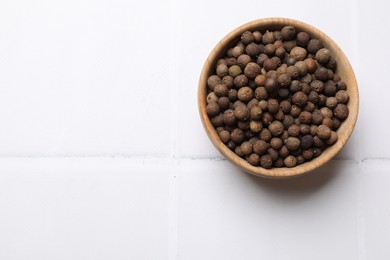 Photo of Dry allspice berries (Jamaica pepper) on white tiled table, top view. Space for text