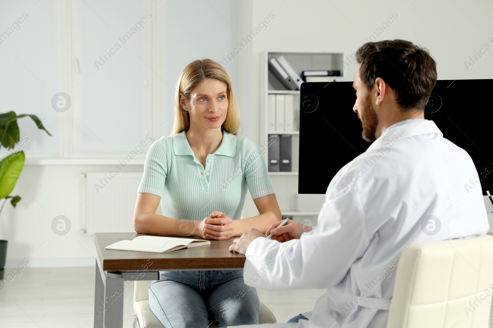 Photo of Doctor consulting patient at wooden table in clinic