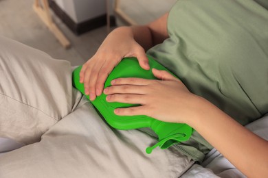 Photo of Young woman using hot water bottle to relieve cystitis pain on bed indoors, closeup
