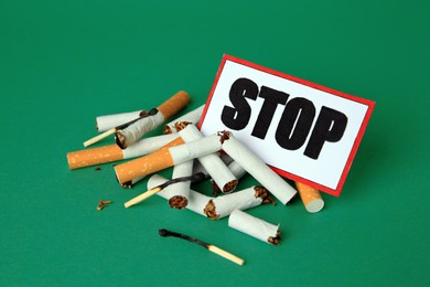 Photo of Card with word Stop, cigarette stubs and burnt matches on green background. Stop smoking concept