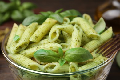 Photo of Bowl of delicious pasta with pesto sauce and basil on table, closeup