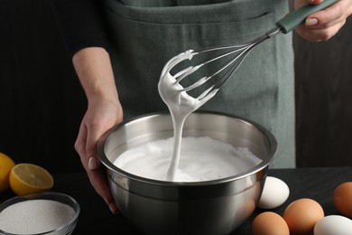 Photo of Woman making whipped cream with whisk at black table, closeup