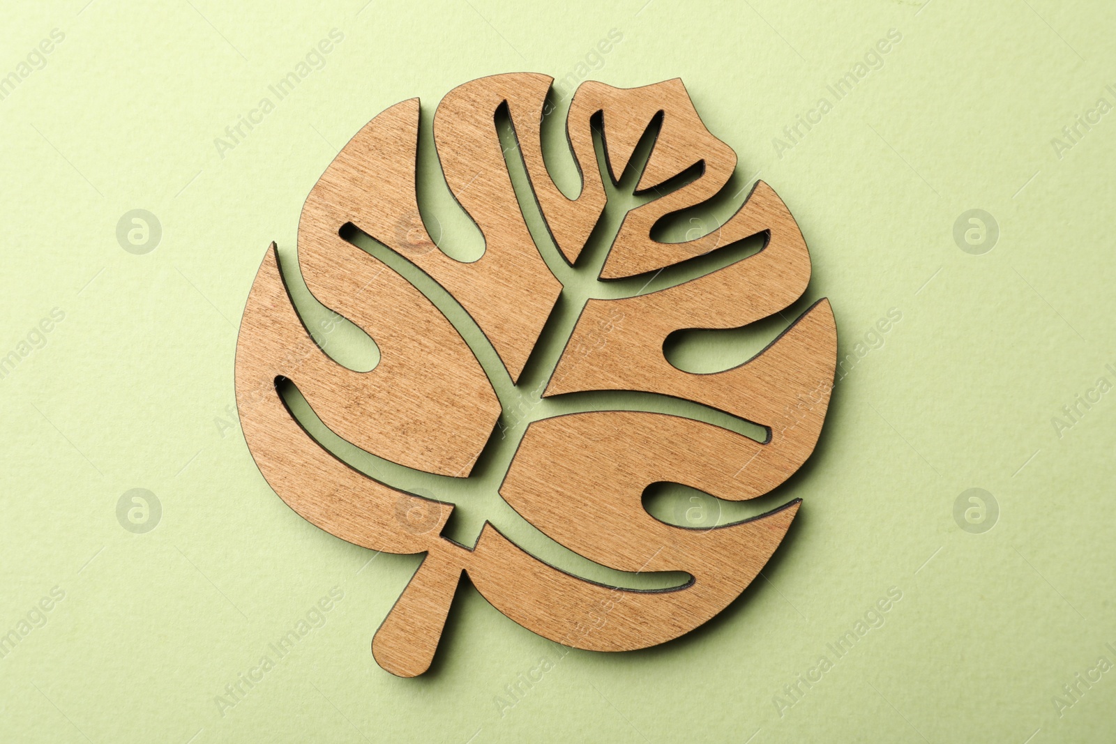 Photo of Leaf shaped wooden cup coaster on green background, top view