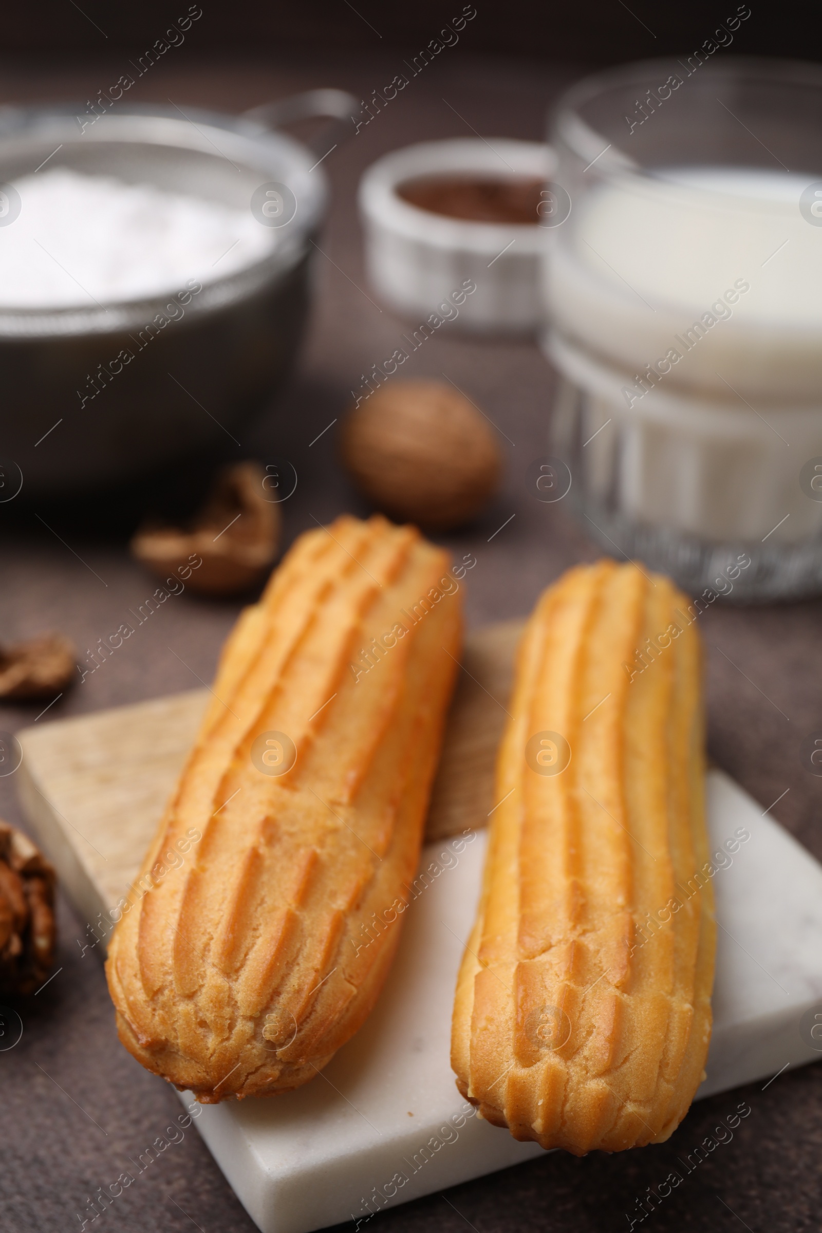 Photo of Delicious eclairs, walnuts and milk on grey table, closeup