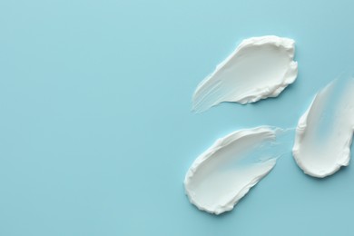 Photo of Samples of face cream on light blue background, top view. Space for text