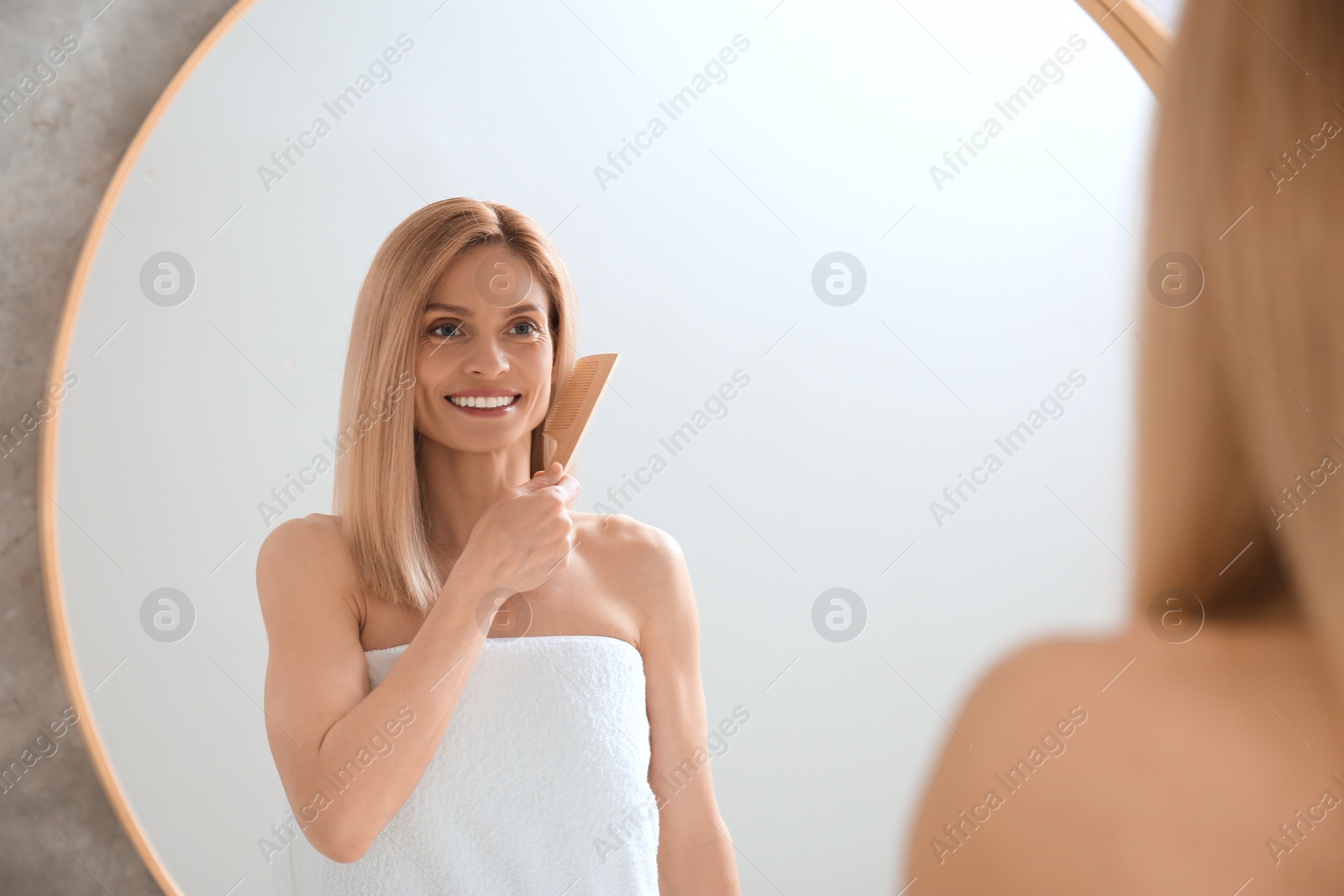 Photo of Beautiful woman brushing her hair near mirror in bathroom