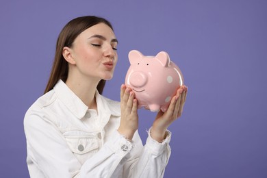 Woman with piggy bank on purple background, space for text