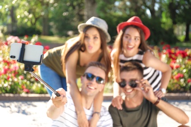 Photo of Group of young people taking selfie with monopod outdoors, focus on smartphone