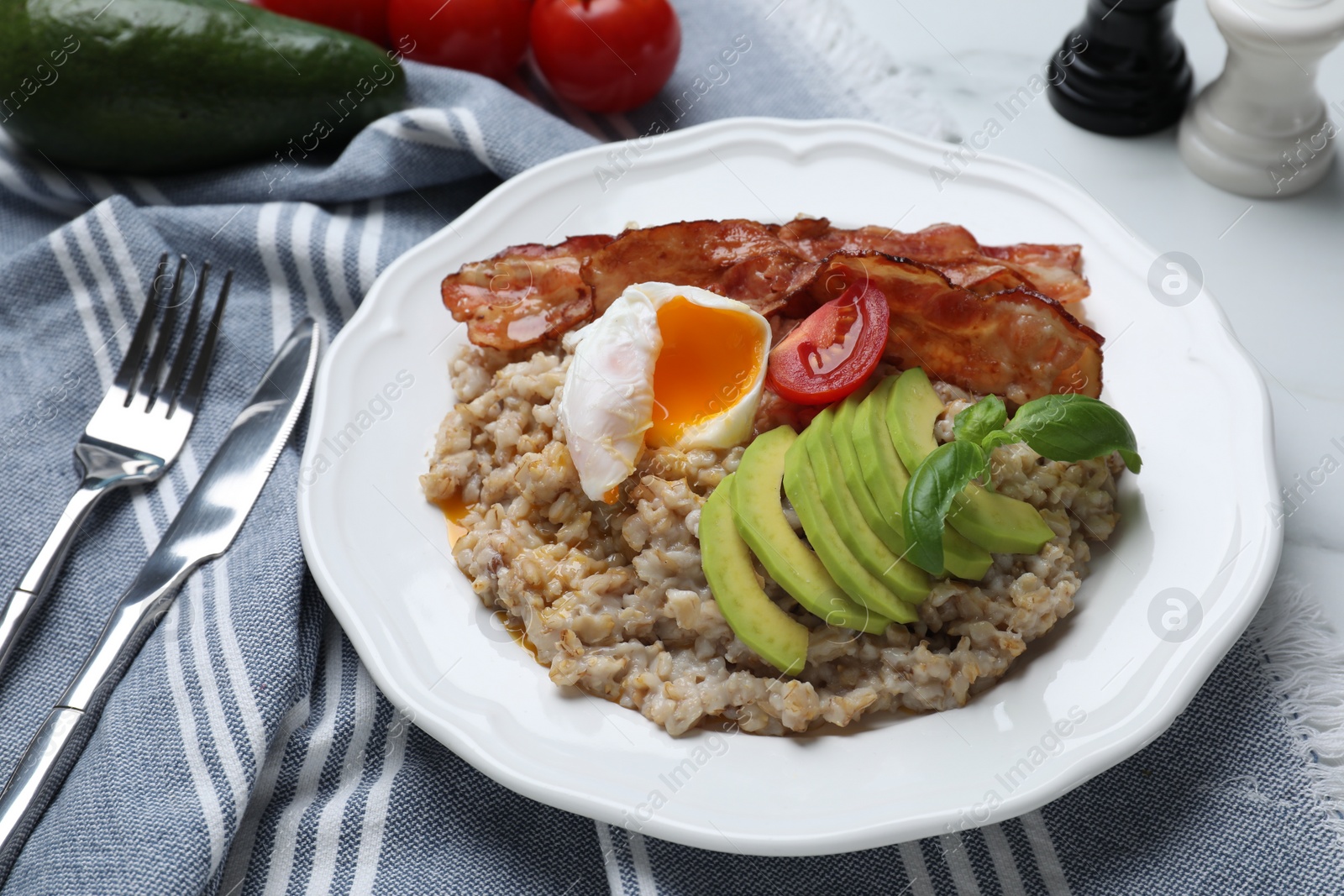 Photo of Delicious boiled oatmeal with egg, bacon, tomato and avocado served on table