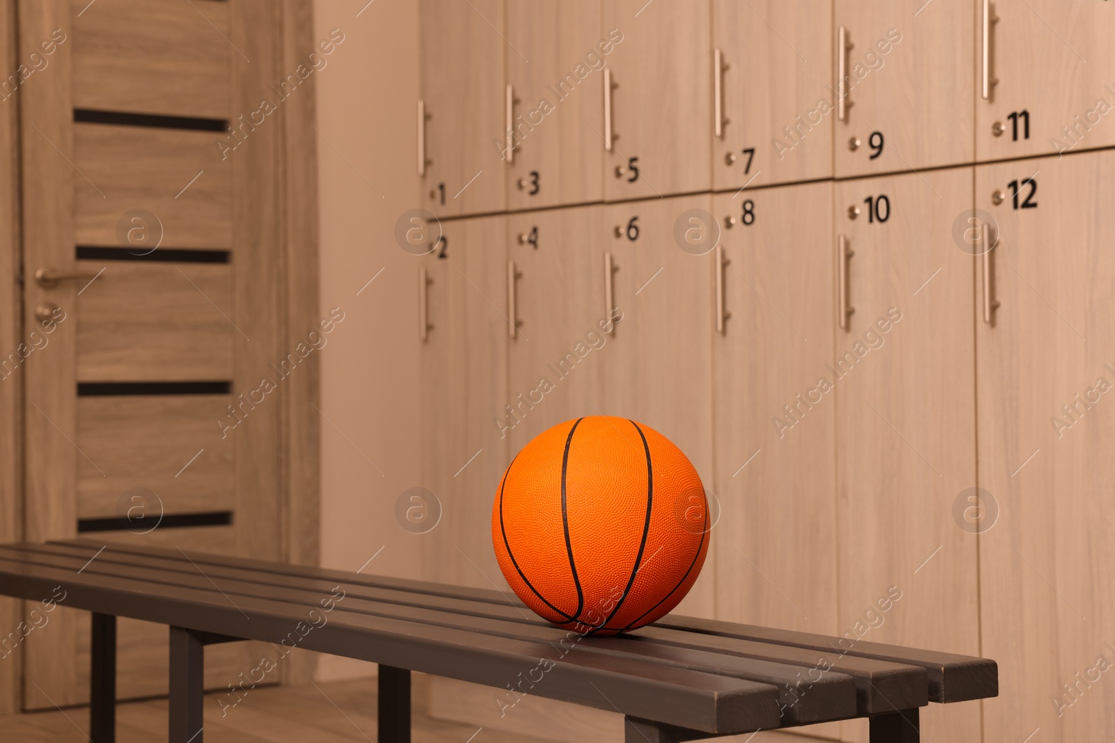 Photo of Orange basketball ball on wooden bench in locker room