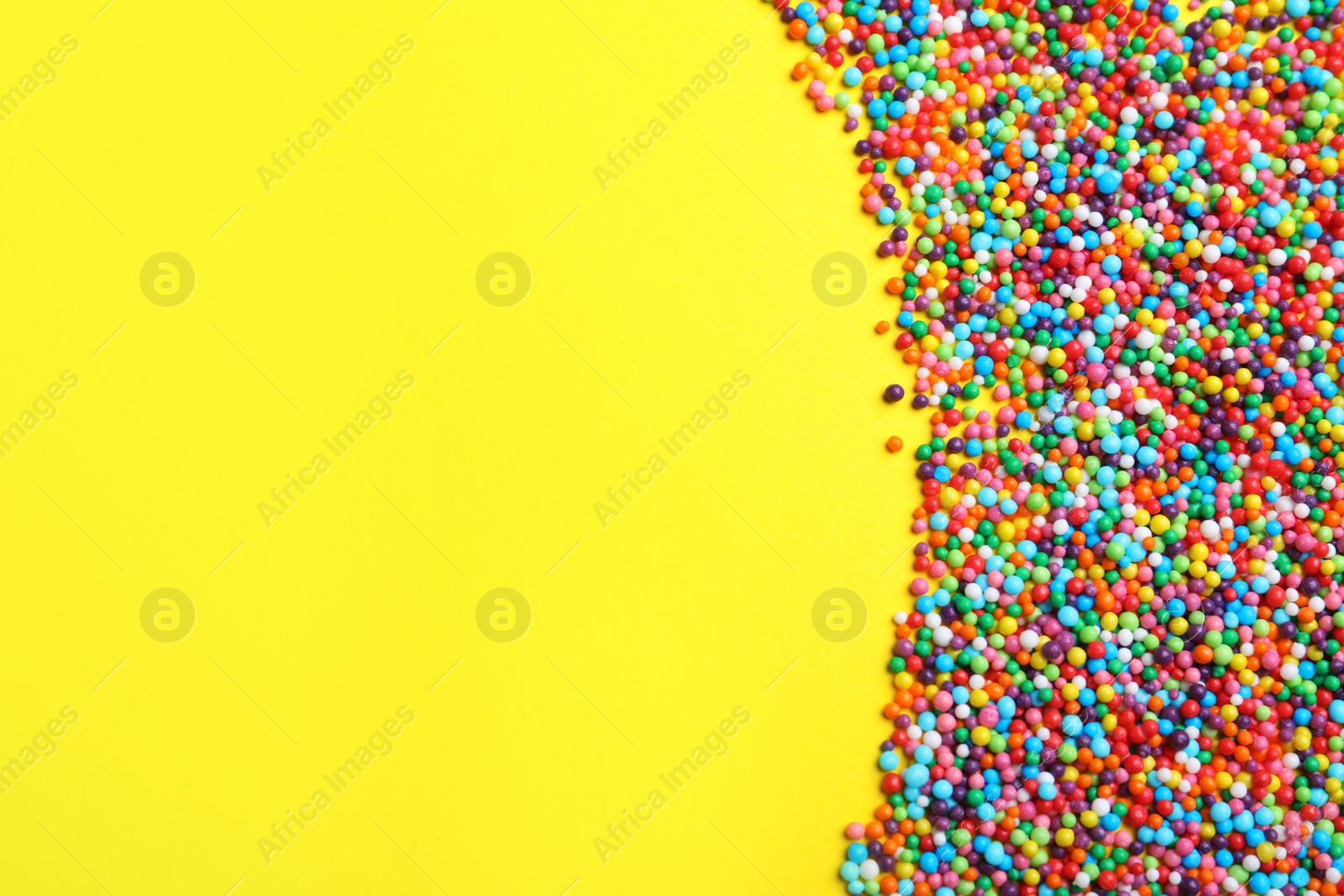 Photo of Bright colorful sprinkles on yellow background, flat lay with space for text. Confectionery decor