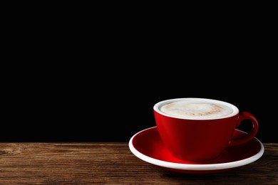 Photo of Red cup with aromatic cappuccino on wooden table against black background. Space for text