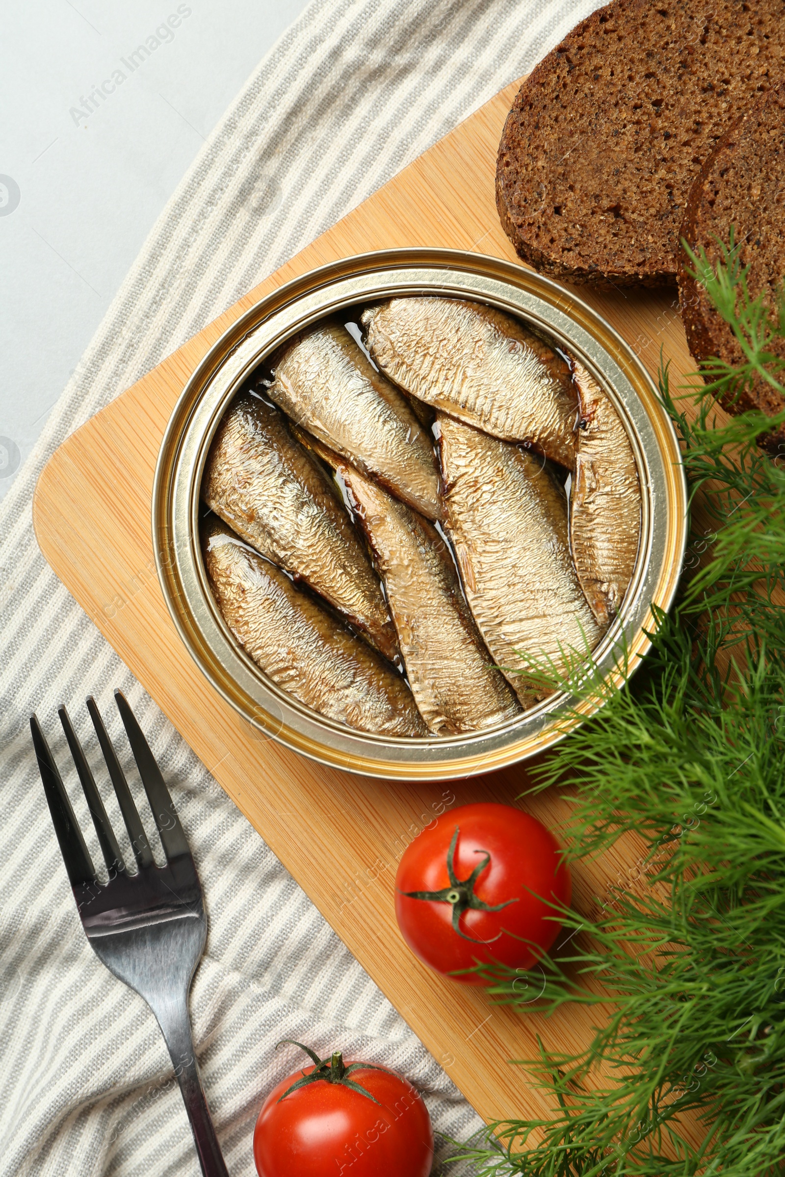 Photo of Canned sprats, dill, tomatoes, bread and fork on light table, flat lay
