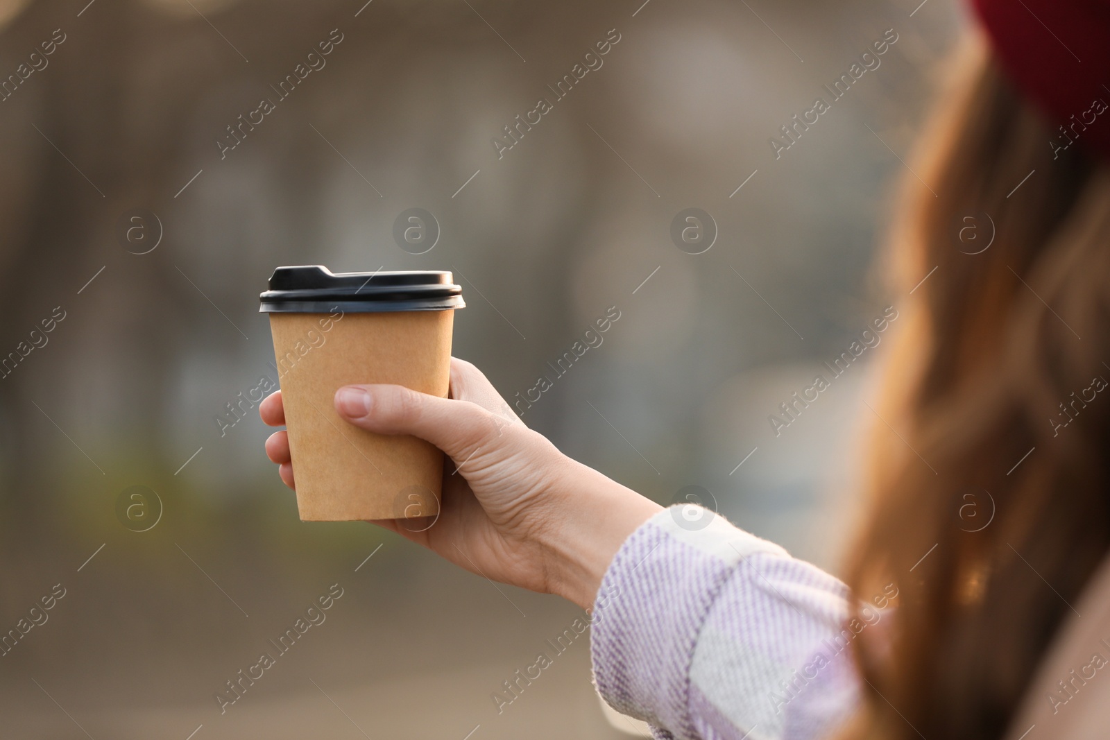 Photo of Woman holding paper coffee cup outdoors, closeup