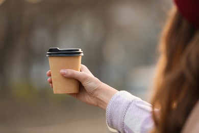 Woman holding paper coffee cup outdoors, closeup